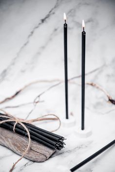 two black candles sitting on top of a white marble table next to twine of sticks