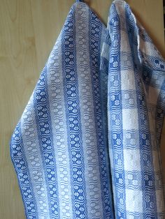 two blue and white cloths folded on top of each other in front of a wooden table