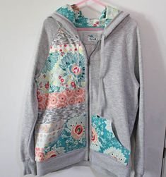 a gray hoodie with floral print on the front and back, hanging up against a white wall