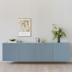 a blue sideboard with vases and flowers on it in front of a white wall