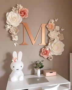 a white desk topped with a laptop computer next to a pink flower wall letter m