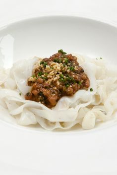 a white bowl filled with noodles and meat covered in sauce on top of a table