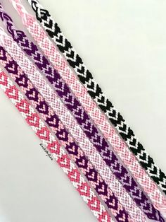 four braided bracelets in different colors and patterns on a white surface with black, pink, and purple thread