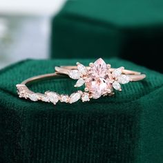 a pink diamond ring sitting on top of a green velvet cushioned box with white diamonds surrounding it