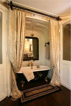 a bath tub sitting under a bathroom mirror next to a window with curtains on it