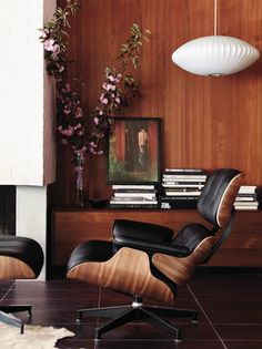 an eames chair and ottoman in front of a wood paneled wall with pictures on it