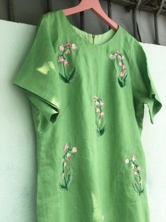 a green shirt with pink flowers on it hanging from a hanger next to a white wall