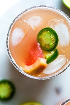 two glasses filled with drinks and garnished with limes next to sliced kiwi