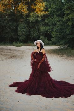 a woman in a dress and hat standing on the sand with trees in the background