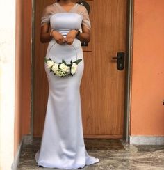 a woman standing in front of a door wearing a white dress and holding a flower bouquet