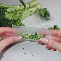 two hands holding a piece of paper with broccoli on it next to another person's hand