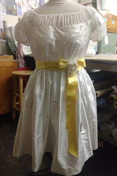 We are unusually busy this year, so custom sizes require a THREE MONTH wait.  Your costume will not be made until late October, and it will NOT ARRIVE IN TIME FOR HALLOWEEN!!!We are so excited to finally be making this gorgeous dress!  It is a replica of the winter white silk dress with yellow bow that Liesl wears to the ball in the Sound of Music. Extra full 100% silk skirt, yellow satin sash, and hand beaded bodice. The body of the dress is real Shantung silk, and the sheer part is real silk c White Wedding Dress With Sashes, Fitted Dress With Bow For Confirmation, White Formal Dresses With Sashes, Formal White Dresses With Satin Bow, Regency Style White Dress For Debutante Ball, Fitted Yellow Dress For Debutante Ball, Formal White Dress With Ribbon, White Formal Dress With Satin Bow, Yellow Fitted Dress For Debutante Ball