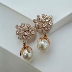 Make a stunning statement this season with the gorgeous Flowers Pearl Earrings. These elegant earrings feature an exquisite floral-inspired design for timeless sophistication. Three delicate blossoms set as if in a bouquet boast an abundance of dazzling cubic zirconia on each petal with a beautiful pearl dangling provocatively beneath, giving it an extra special touch of sophistication. Pearls are an elegant, classic choice that will never go out of style. This timeless gemstone will take you to every significant event of your life. Whether you're the stylish bride with a taste for timeless elegance, or just wanting to add a dash of sparkle to your everyday wardrobe, these earrings will be all you need. Handcrafted in 925 sterling silver dipped in 18ct rosegold. Pearls. Cubic zirconia.  Pa Luxury Rose Gold Pearl Drop Earrings, Rose Gold Pearl Drop Flower Earrings, Luxury Rose Gold Drop Pearl Earrings, Formal Rose Gold Pearl Earrings With Elegant Design, Rose Gold Flower Drop Earrings With Pearl, Formal Rose Gold Earrings With Rose Design, Luxury Drop Flower Earrings For Wedding, Luxury Flower Drop Earrings For Wedding, Formal Rose Gold Flower Earrings