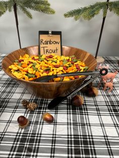 a wooden bowl filled with fruit on top of a checkered table cloth next to pine trees