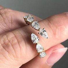 a woman's hand holding three diamond earrings on top of her finger, with the middle