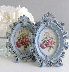 two small blue frames with pink and white flowers on them next to a crystal vase