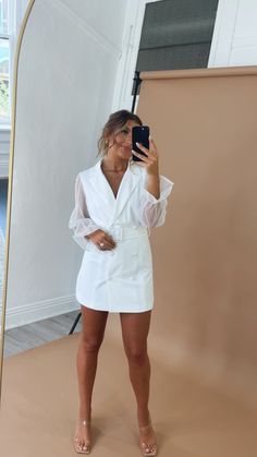 a woman taking a selfie in front of a mirror wearing a white shirt dress