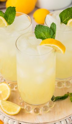 two glasses filled with lemonade and mint garnish on a tray surrounded by lemons