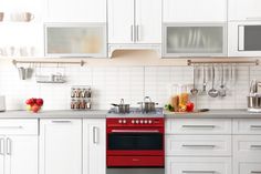 a red stove top oven sitting inside of a kitchen next to white cabinets and drawers