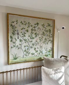 a white pillow sitting on top of a bed next to a wall hanging with birds and flowers