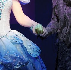 a woman in a blue and white dress holding hands with a man dressed as the beast