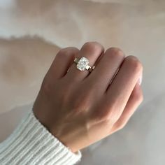 a woman's hand with a diamond ring on top of her finger, wearing a white sweater