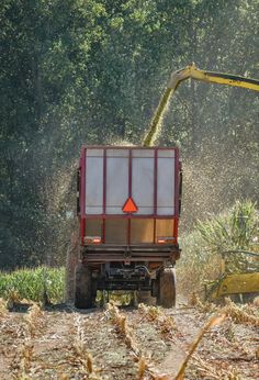 a red truck driving down a dirt road next to a green machine and some trees