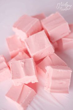 some pink marshmallows are on a white plate and have been cut into squares