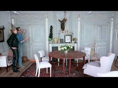 two people are standing in the middle of a room with white chairs and a round table