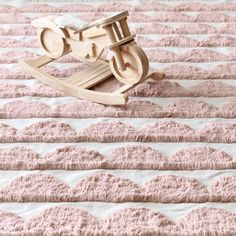 a wooden rocking toy sitting on top of a pink bed sheet covered in white stripes