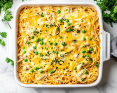 a casserole dish with chicken, peas and cheese in it on a marble surface