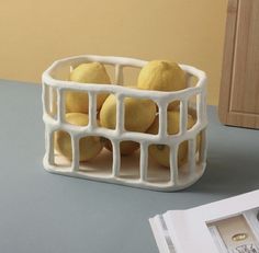 some lemons are in a white basket on a table next to an open magazine