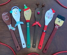 five wooden spoons are decorated with paper animals and faces, along with red string on the table