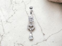 a pair of dangling belly rings with heart and crystal stones in the center on a marble surface