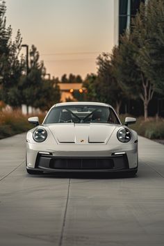 a white sports car parked in front of a tall building with trees on the other side