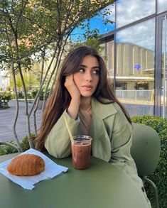 a woman sitting at a table with a drink and croissant in front of her