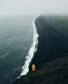 a person standing on the edge of a cliff overlooking the ocean with waves coming in