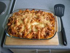 a casserole dish with meat and cheese in it on a wooden cutting board