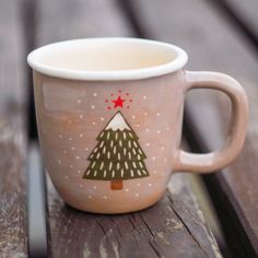 a coffee cup with a christmas tree painted on it sitting on a wooden table next to a tabletop