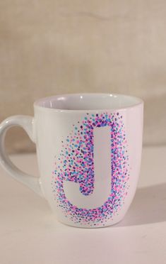 a white coffee cup with purple and blue sprinkles on the side, in front of a beige background