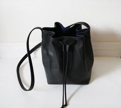 "This bucket bag features soft black leather, cotton lining and a drawstring closure. Carry your phone, a wallet, keys and small items in this bag. Details: -Dimensions: 10.5\" length (top to bottom), 13.5\" opening top width, 6\" depth, 7.5\" X 6\" base (bottom) -Shoulder strap measures approx. 45-50\" total (shoulder strap is adjustable) -Soft black leather -Cotton lining -One internal pocket Hardware color: -Silver (pictured) -Gold Options: -Real cowhide leather (pictured) -Vegan (fake) leath Cheap Black Bucket Bag With Double Handle, Black Leather Bucket Bag With Leather Handles, Black Leather-handled Bucket Bag, Daily Use Bucket Bag With Snap Closure, Black Bucket Bag With Leather Handles, Everyday Pouch Bucket Bag, Black Pouch Bucket Bag For Everyday Use, Black Bucket Bag With Snap Closure, Black Soft Leather Pouch Bucket Bag