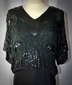 A vintage 1980s retro Edwardian style black 100% silk chiffon pullover blouse with black beading and sequins.  The blouse has a V neckline and wide elbow-length sleeves.  It is a cropped length, with an elastic pulled through a casing at the waist, falling a little higher in the front than the back.  The blouse is fully lined with black silk.  I found no noticeable loose or missing beads or sequins.  38 Inch bust, 34 inches at the waist stretching to 36 inches, 19 inches in length from the shoul Vintage V-neck Blouse For Party, Vintage V-neck Party Blouse, Vintage Embellished Evening Blouse, Vintage V-neck Blouse For Evening, Embellished Black Tops For Cocktail, Black Embellished Evening Blouse, Black Embellished Blouse For Evening, Vintage Beaded Evening Tops, Black Beaded Blouse For Party