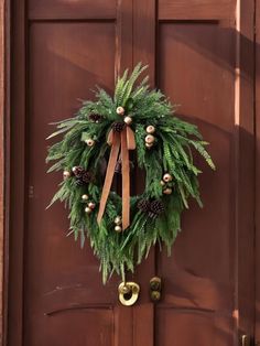 a green wreath with pine cones and bells hangs on the front door of a house