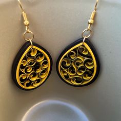 two pairs of earrings with black and gold designs on them sitting on a white surface