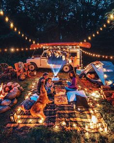 a group of people sitting on top of a blanket next to a campfire with lights