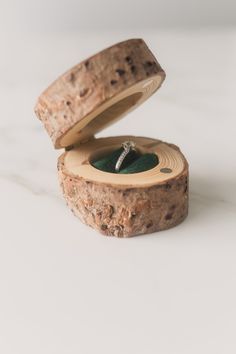 an engagement ring sits in a wooden box on top of a piece of tree bark