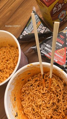 two bowls of ramen with chopsticks in them on a table next to packets of noodles