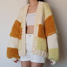 a woman standing in front of a white wall wearing a yellow and brown striped cardigan