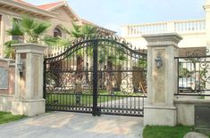 an iron gate in front of a house with palm trees on the lawn and stone steps leading up to it