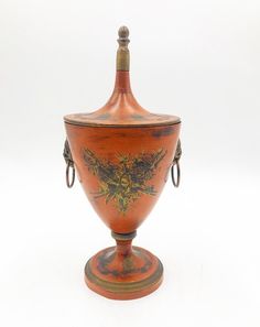 an orange vase with designs on it sitting on a white surface, against a plain background